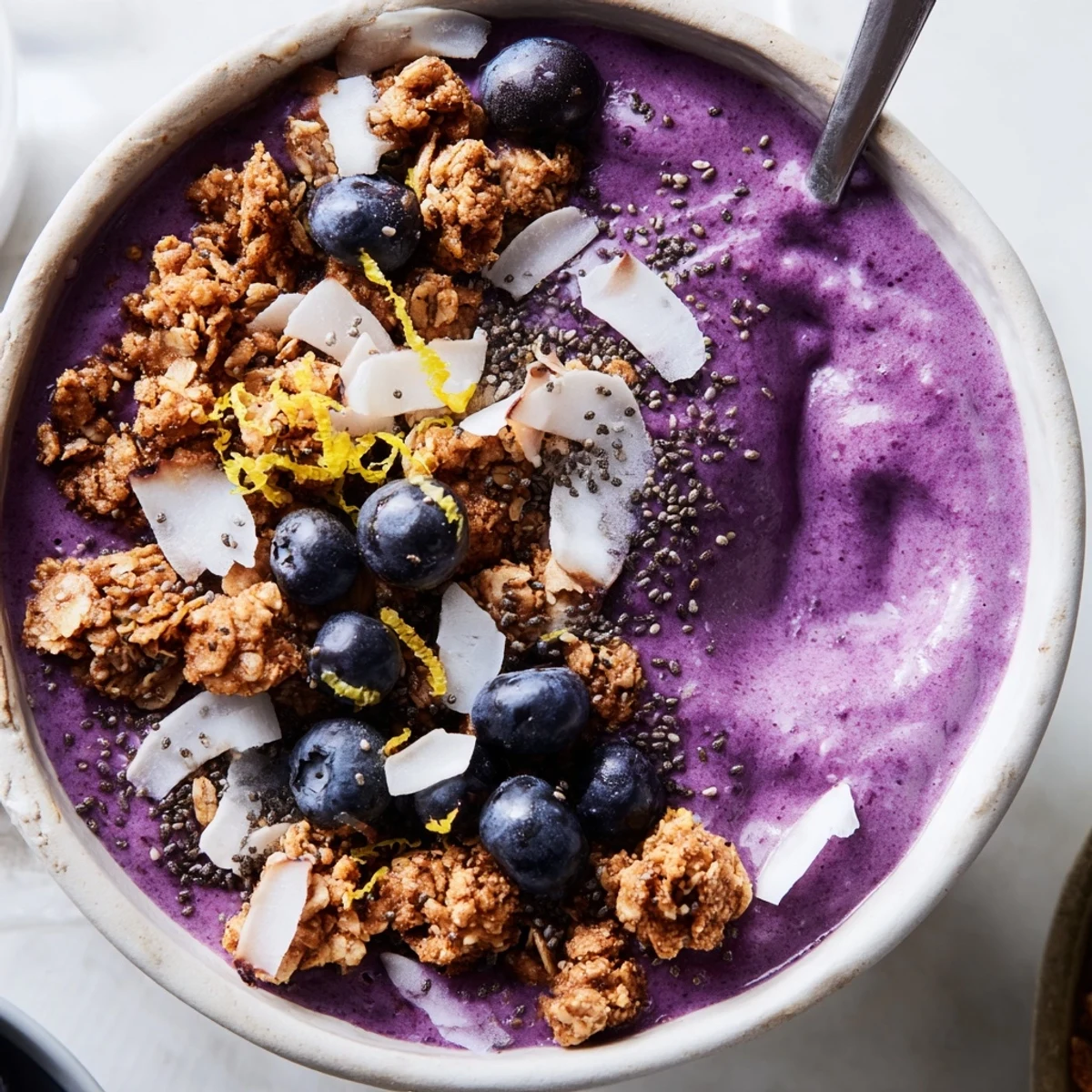 Bright, purple smoothie bowl topped with granola, fresh blueberries, and coconut flakes for a healthy breakfast.