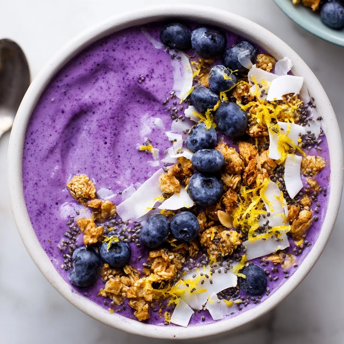 Thick and creamy Lemon Blueberry Smoothie Bowl served in a white ceramic bowl with a spoon nearby.