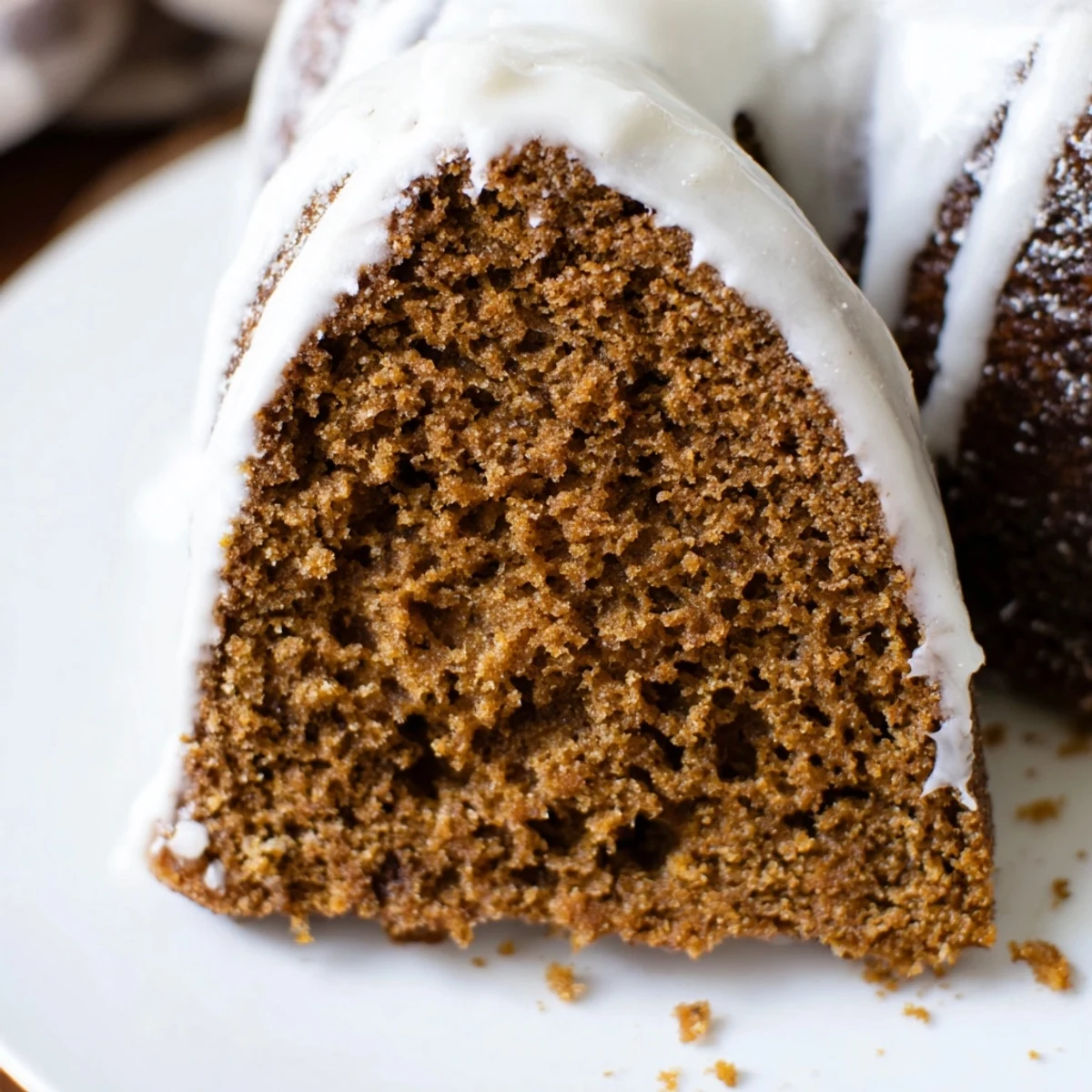 Slice of Gingerbread Spiced Bundt Cake on a white plate, revealing a moist crumb next to a warm cup of coffee.