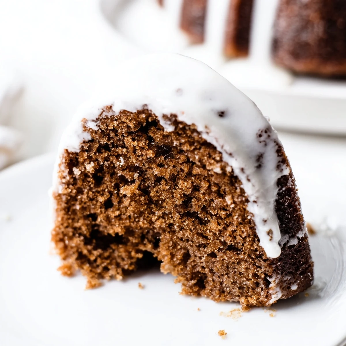 Freshly baked Gingerbread Spiced Bundt Cake with glaze dripping down the ridges, served on a rustic wooden board.