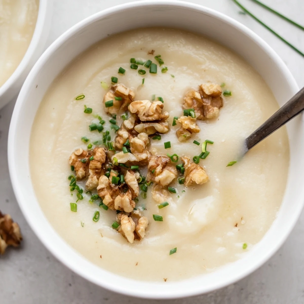 Creamy parsnip and pear soup steaming in a rustic bowl with golden toasted walnuts and fresh green chives.