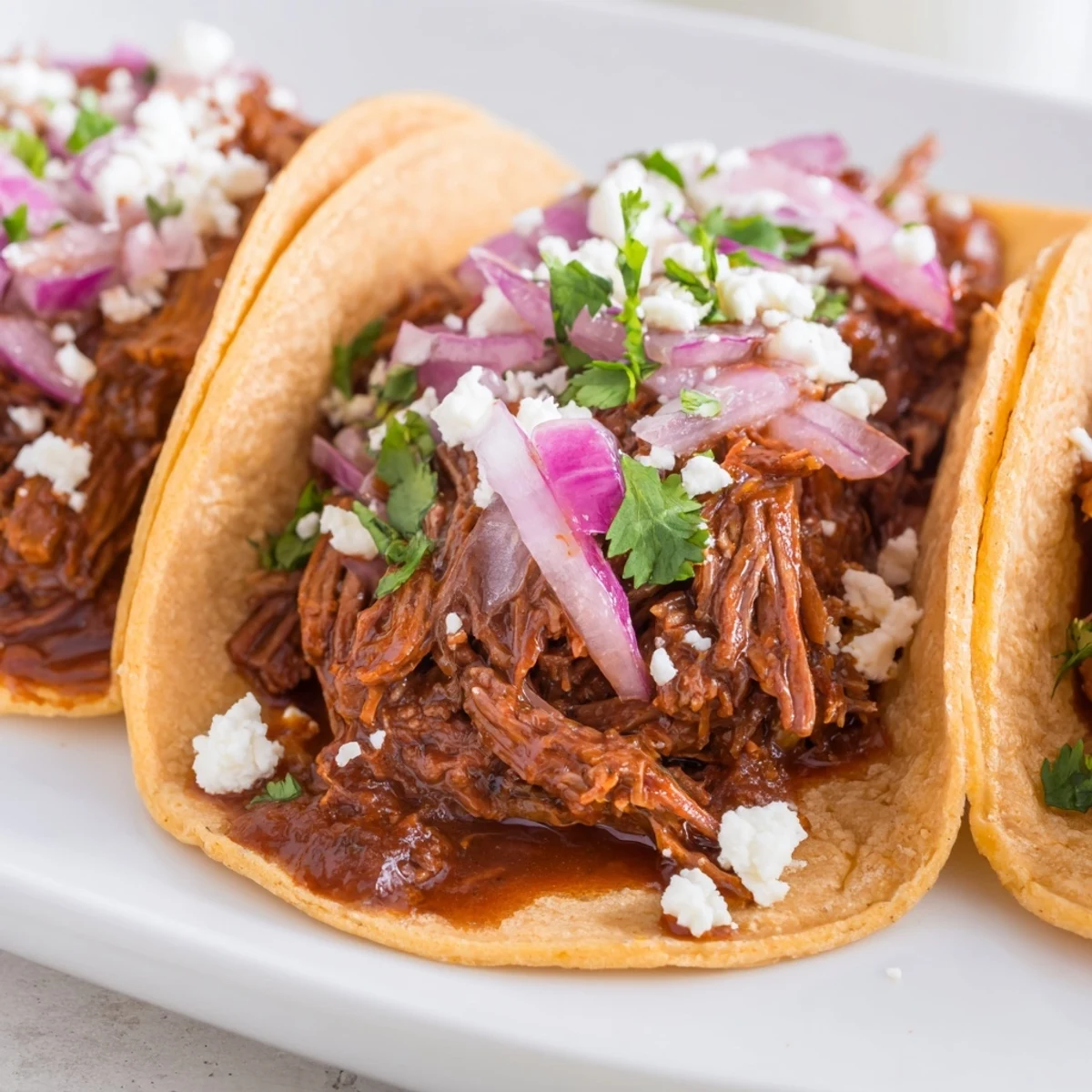 Tender, juicy shredded beef fills warm corn tortillas, topped with fresh cilantro, diced red onion, and crumbled queso fresco.