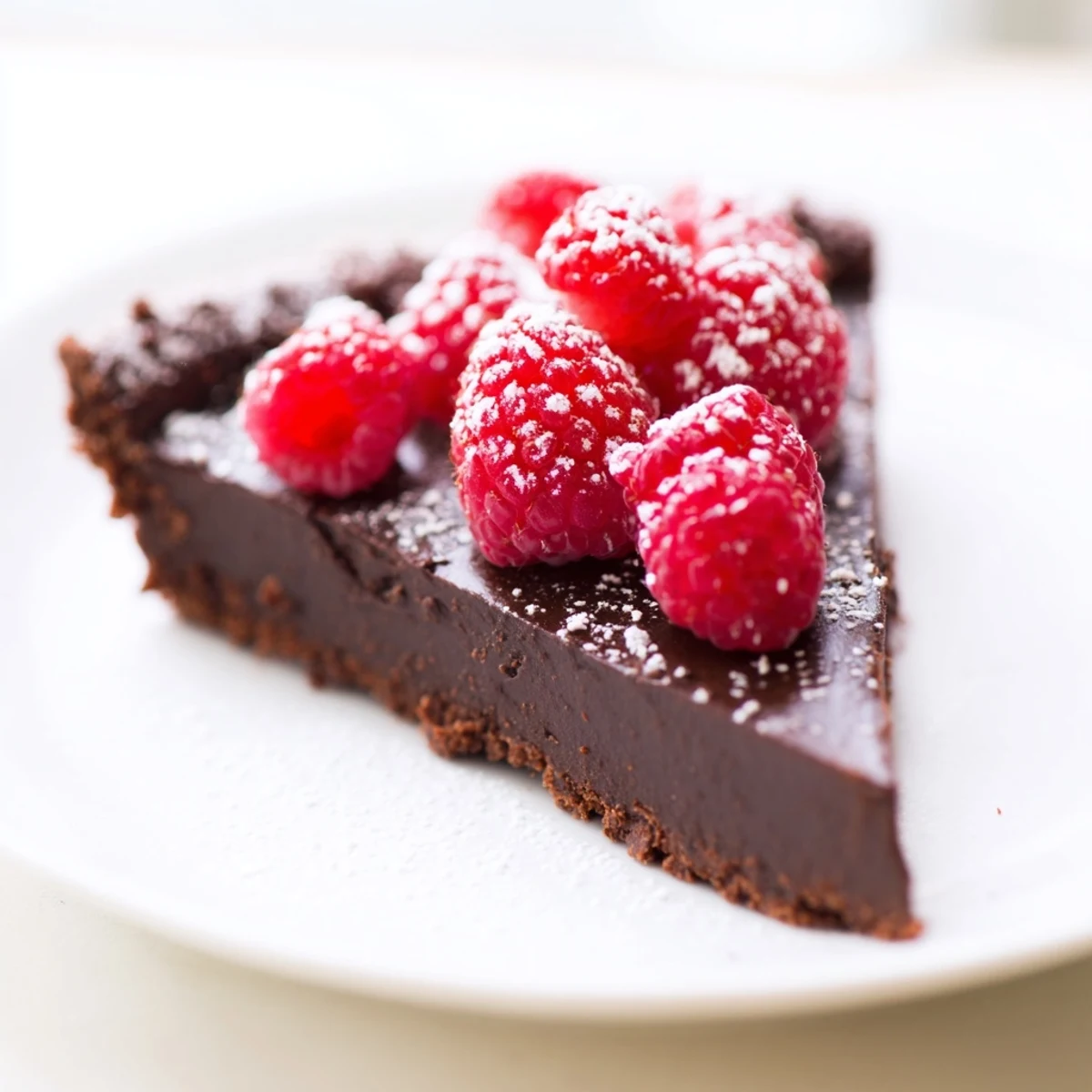 A close-up of Decadent Dark Chocolate Tart with Raspberries reveals glossy ganache and plump raspberries on a buttery chocolate crust.