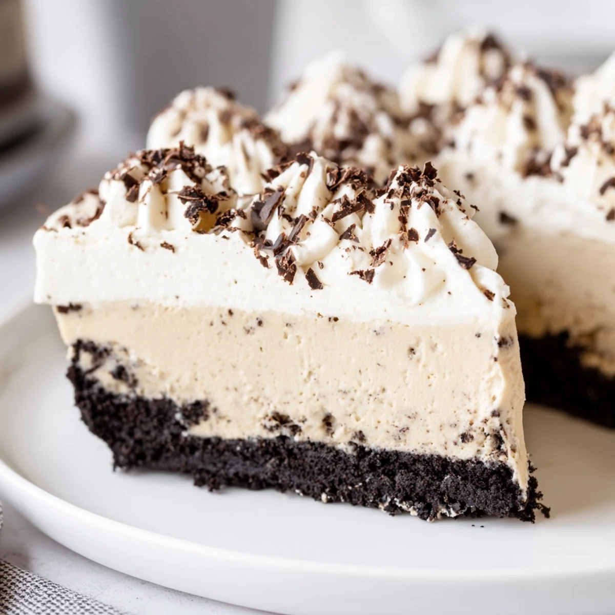 A slice of Bailey Style Irish Cream Cheesecake on a white plate, topped with fluffy whipped cream and dark chocolate shavings.