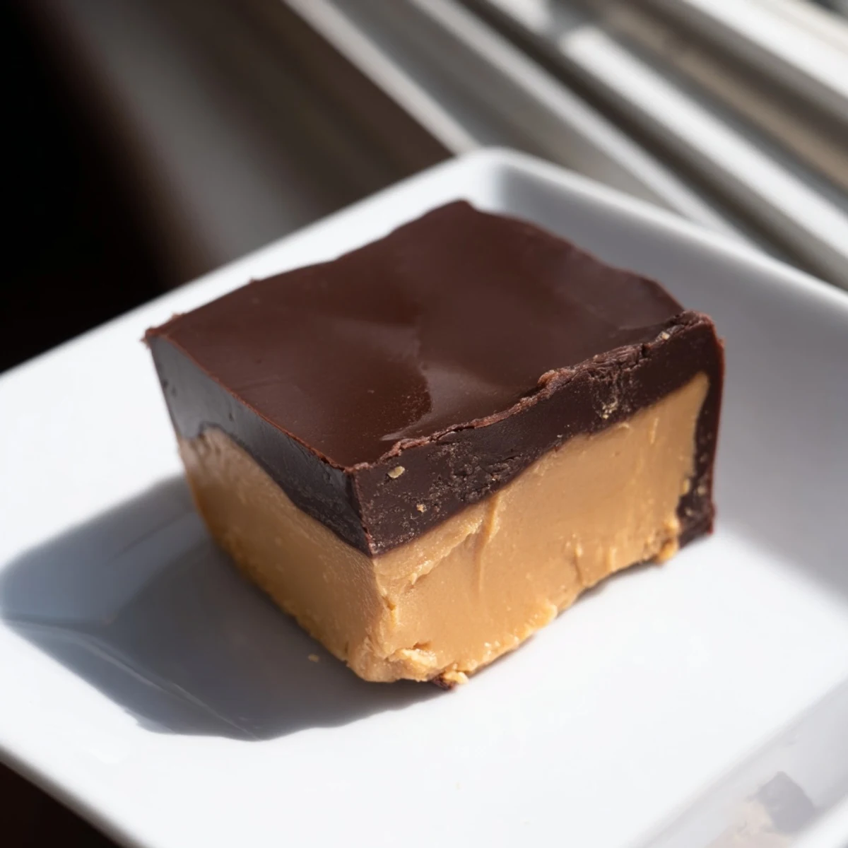 Fudgy chocolate peanut butter fudge squares stacked on a white plate, with a melty bite revealing the creamy layers.  