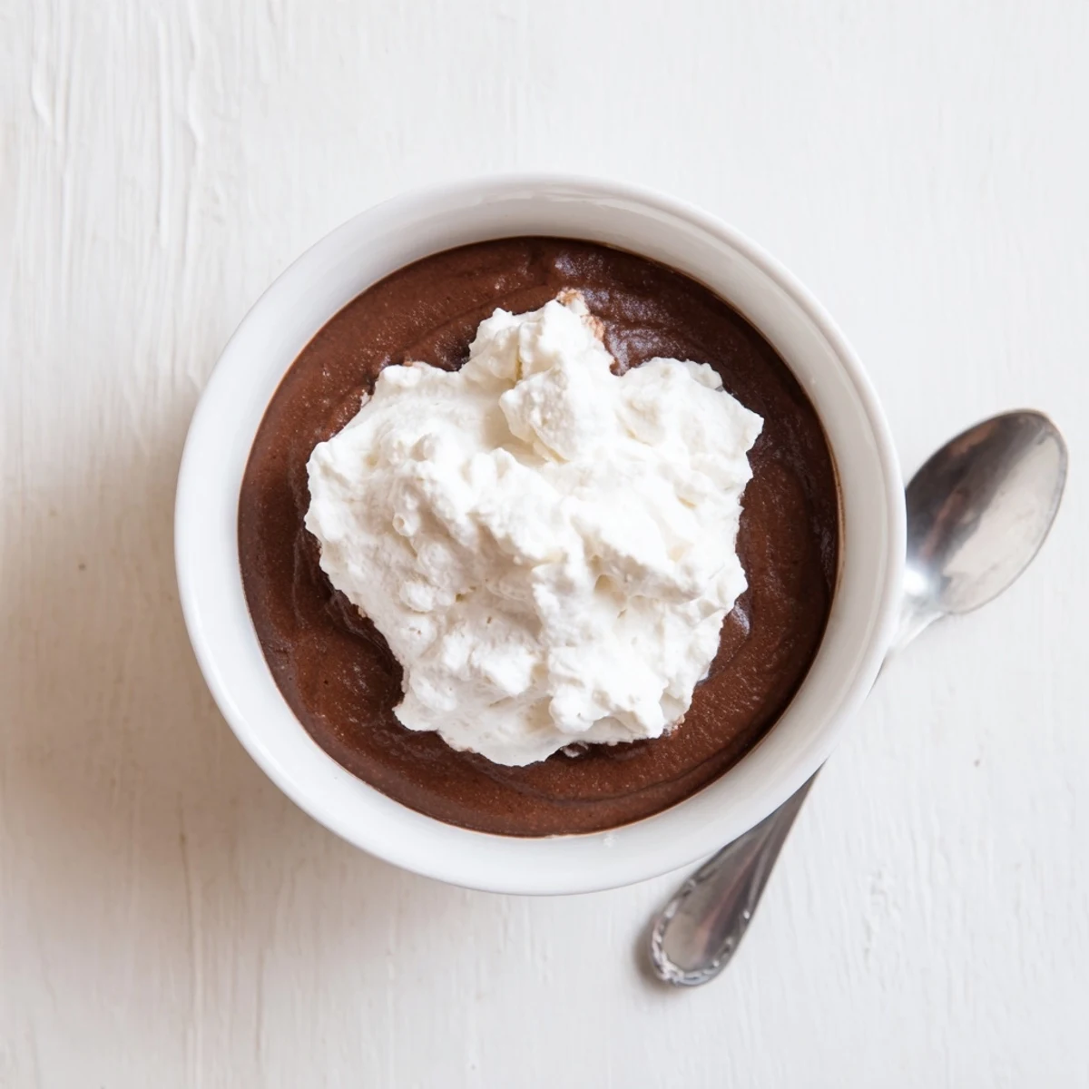 Homemade chocolate pudding with whipped cream in individual ramekins, garnished with chocolate shavings on a rustic table.  