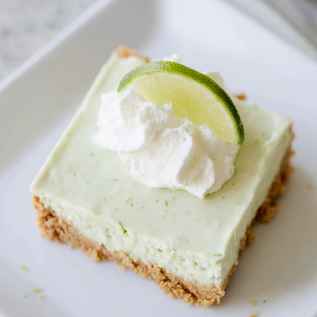 A close-up view of chilled Key Lime Pie Bars, each square topped with a dollop of whipped cream and lime zest.