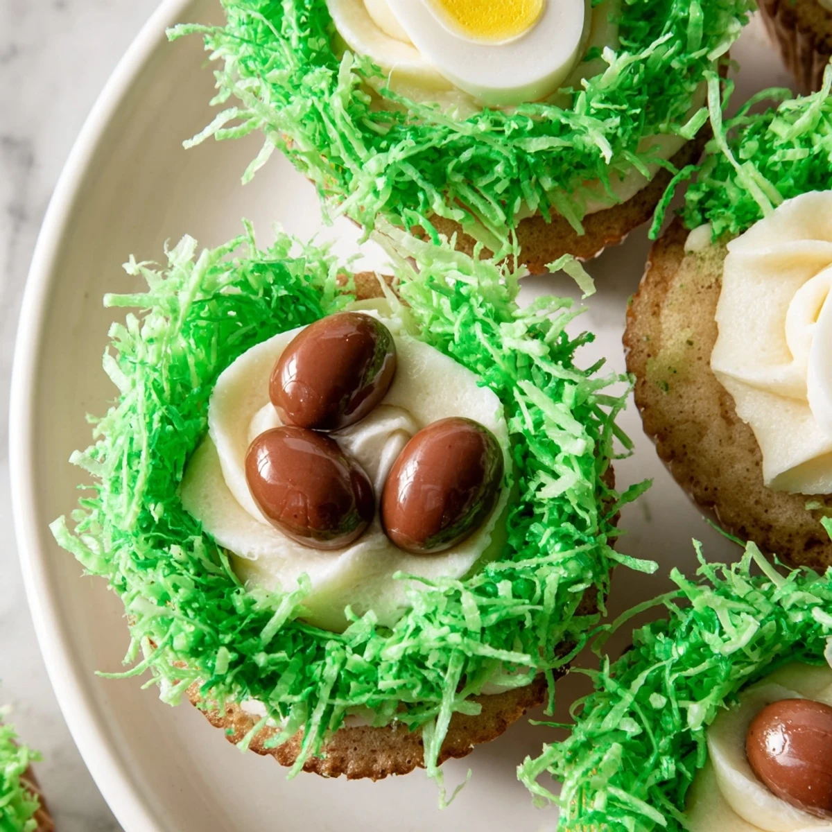 Golden cupcakes topped with green-tinted coconut grass and candy eggs, decorated with candy handles for Easter celebrations.