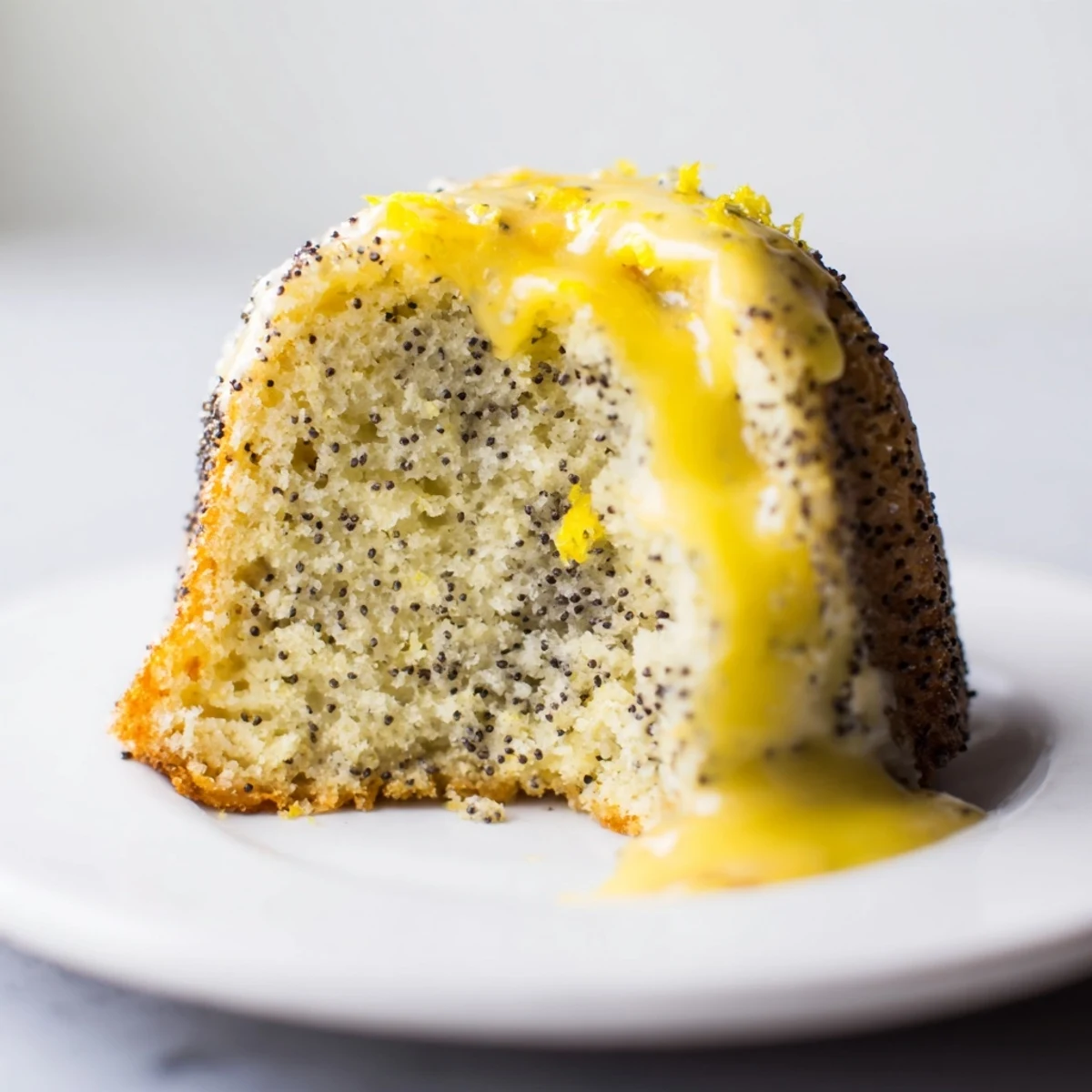 A golden Lemon Poppy Seed Bundt Cake with a glossy lemon glaze dripped down its fluted sides, garnished with fresh lemon zest.