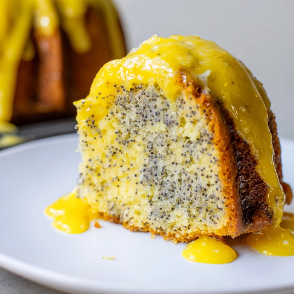 Slices of moist Lemon Poppy Seed Bundt Cake reveal a tender crumb speckled with poppy seeds, served on a ceramic plate.