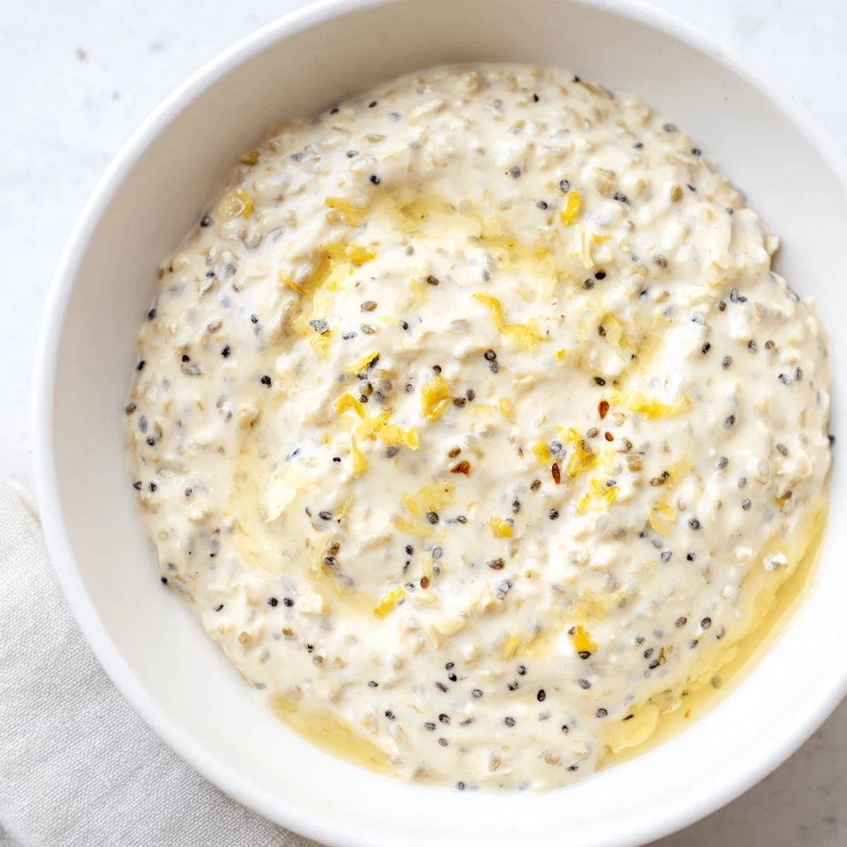 Spoonful of Vegan Lemon Poppy Seed Overnight oats being lifted, revealing a creamy texture with visible poppy seeds.