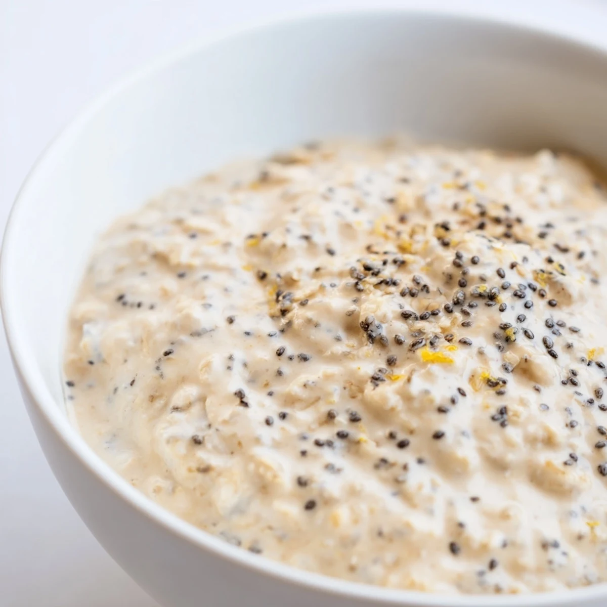 A beautiful serving of Vegan Lemon Poppy Seed Overnight Oats topped with coconut yogurt and fresh berries in a breakfast bowl.
