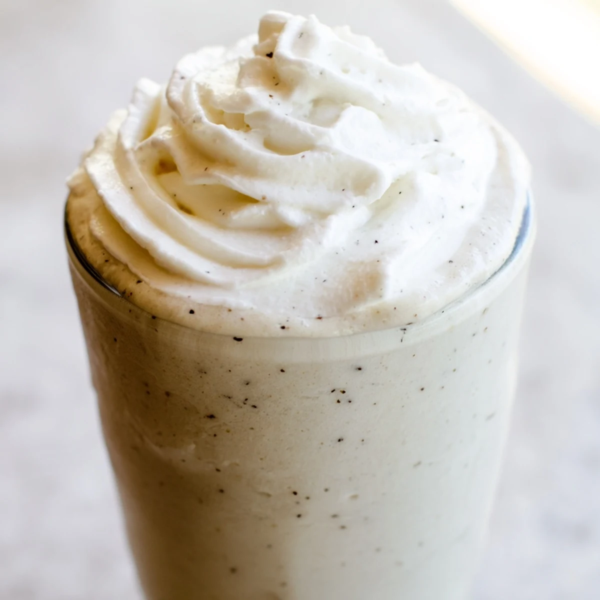 A close-up image of the homemade Starbucks Vanilla Bean Frappuccino, showing ice cubes and vanilla specks in a frosty glass.  