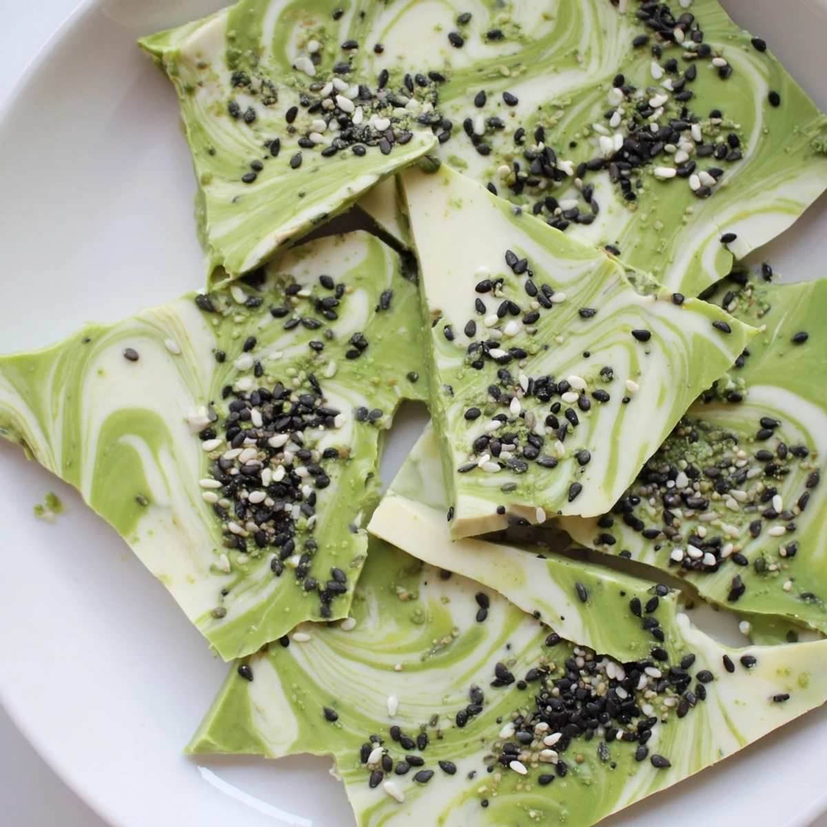 A close-up view of broken Black Sesame Matcha Bark pieces revealing marbled white chocolate and earthy, crunchy black sesame toppings.