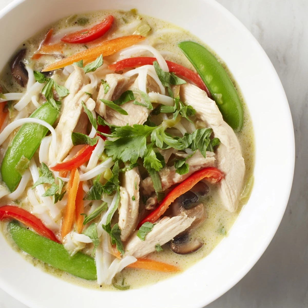 A close-up of Thai Green Curry Chicken Noodle Soup with rice noodles, tender chicken, and vibrant vegetables in creamy broth.
