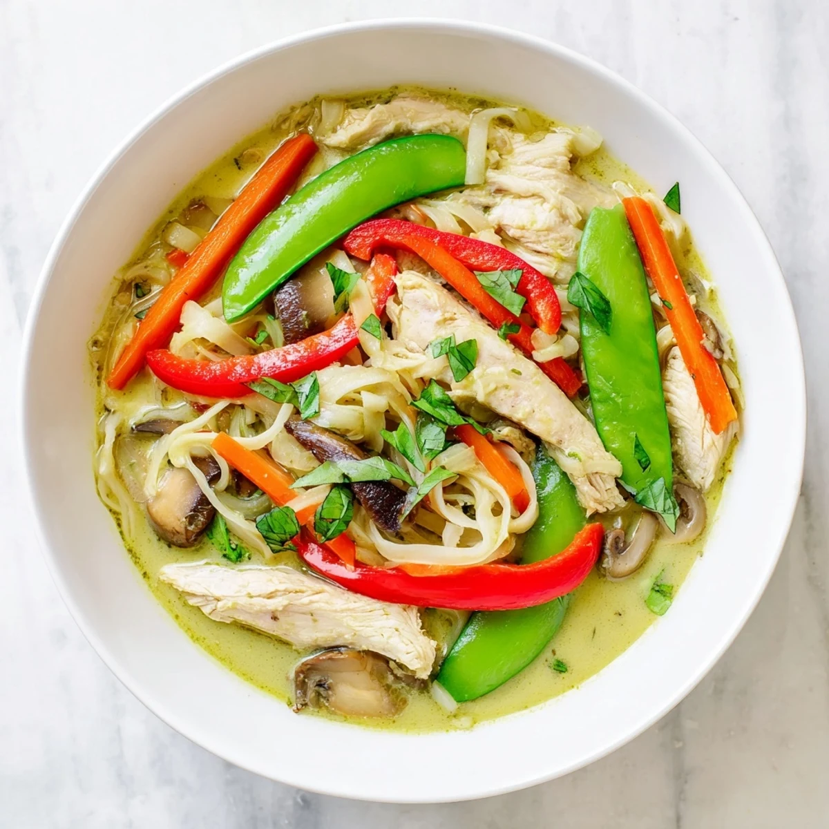 Steam rising from a bowl of Thai Green Curry Chicken Noodle Soup featuring colorful peppers, snap peas, and carrots.