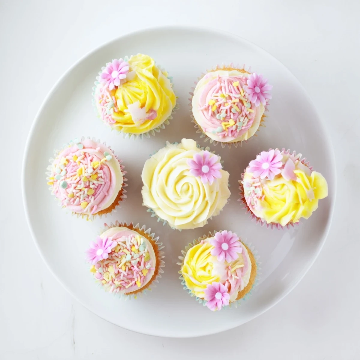 Delicate vanilla Baby In Bloom Cupcakes topped with pastel floral buttercream, displayed on a white platter for a baby shower.