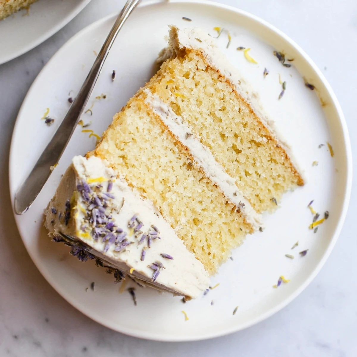 A slice of London Fog Cake with Earl Grey & Lavender displays layers of delicate tea-infused cake with creamy vanilla frosting.