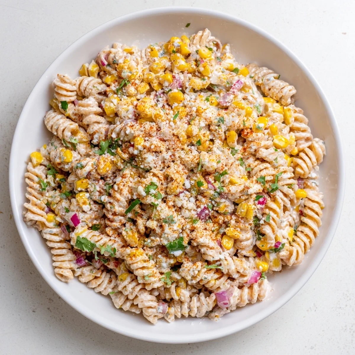 Colorful Mexican street corn pasta salad with sweet corn, creamy cotija cheese and zesty lime dressing in a white serving bowl