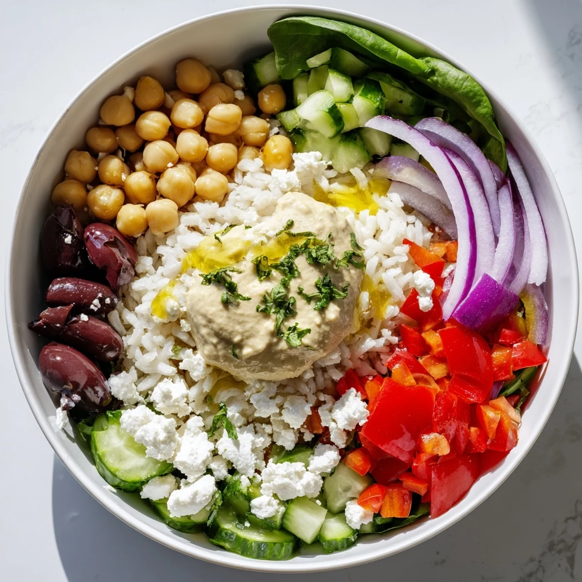 Colorful Mediterranean rice bowl layered with crisp vegetables, creamy hummus, and tangy feta cheese