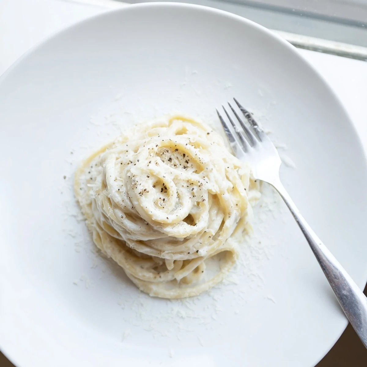 Steaming plate of cacio e pepe pasta featuring glossy cheese sauce and generous black pepper specks
