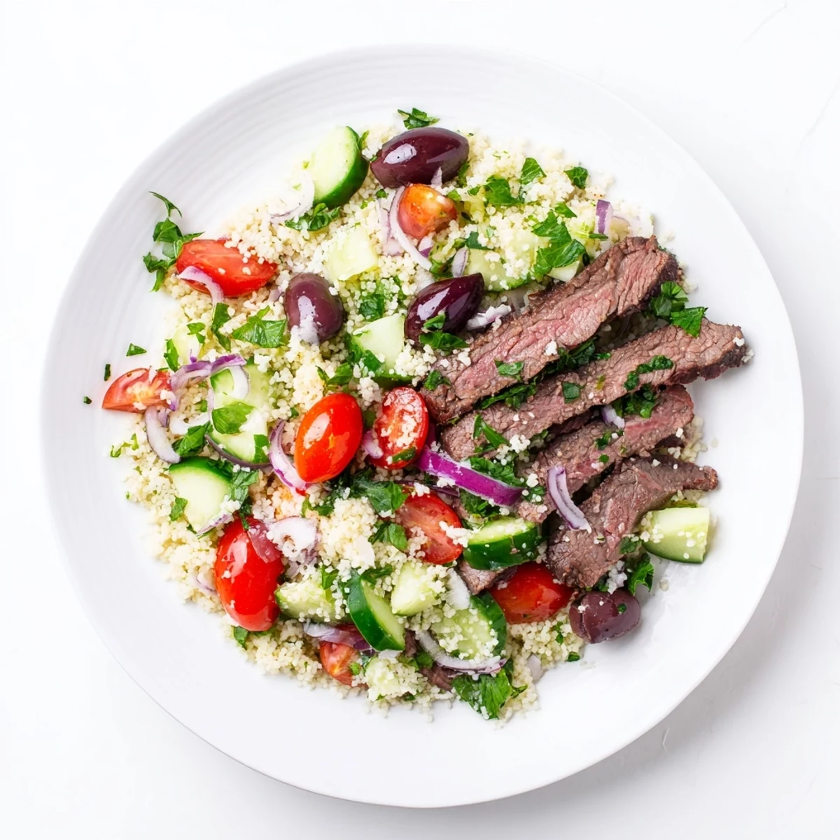 Sliced smoky steak arranged over Mediterranean couscous salad tossed with fresh tomatoes and cucumber