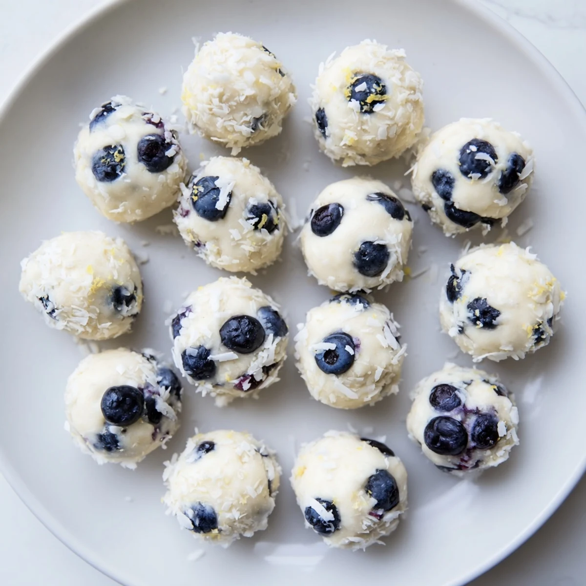 Golden blueberry cheesecake protein bites arranged on a white plate with fresh blueberry garnish