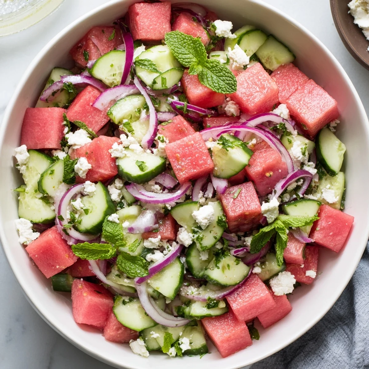 Mediterranean watermelon feta salad arranged on white plate featuring crisp watermelon chunks, creamy feta crumbles, thinly sliced red onion, and fresh green mint garnish
