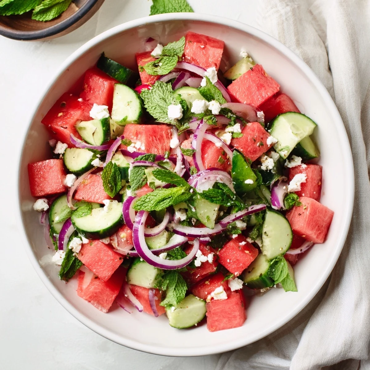 Summer watermelon feta salad close-up displaying vibrant pink watermelon pieces sprinkled with salty feta cheese, diced cucumber, and bright mint leaves in light citrus dressing