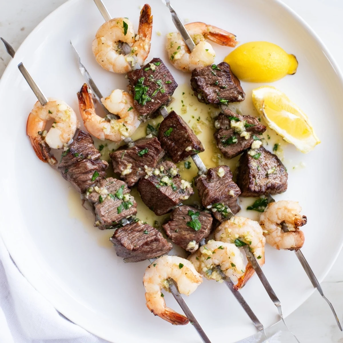 Sizzling garlic butter steak and shrimp skewers garnished with lemon wedges on a platter