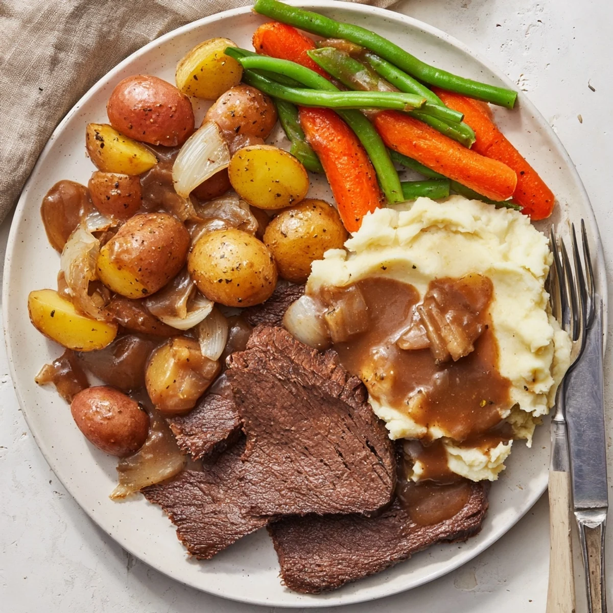 Golden browned Southern style pot roast sliced with roasted vegetables and creamy mashed potatoes on a white dinner plate