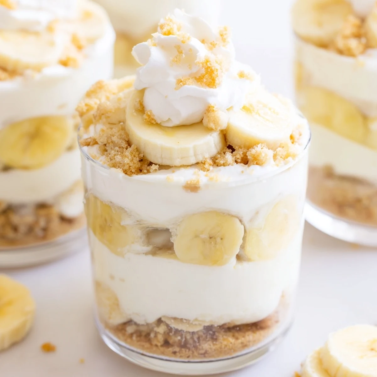 Creamy no bake banana pudding cheesecake cups with layered banana slices and vanilla wafer crumbs in clear glass jars