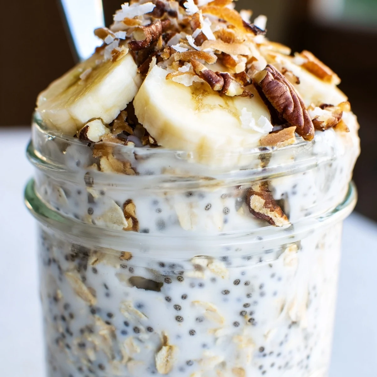 Coconut cream pie overnight oats served chilled with crunchy pecans and fresh banana slices