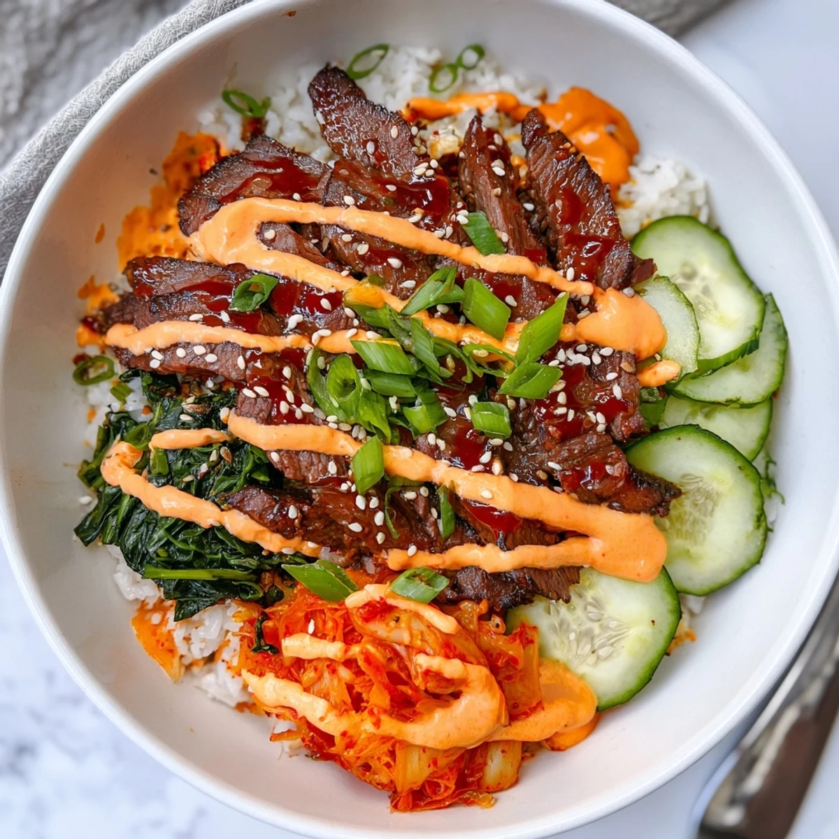 Crisp shredded carrots and chopped kimchi topping savory Korean BBQ steak rice bowls with a creamy sriracha drizzle