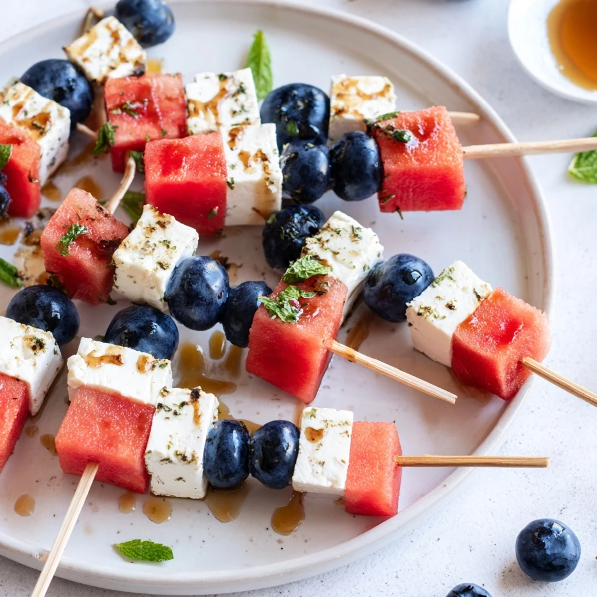 Bright Patriotic Watermelon Feta Skewers threaded with blueberries, mint, and honey drizzle
