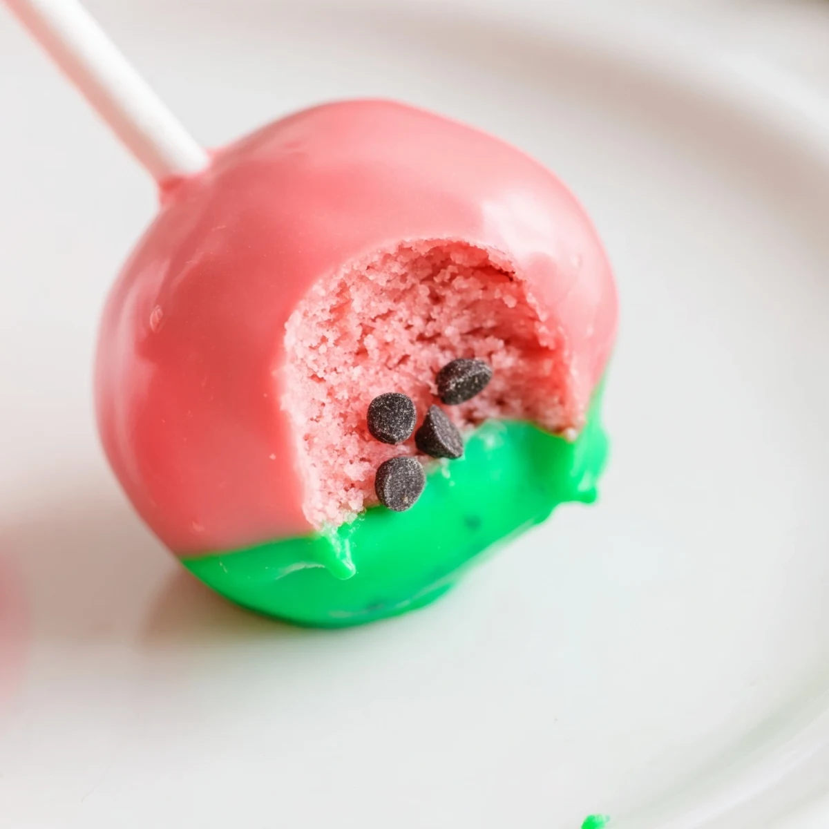 Bite-sized watermelon cake pops on lollipop sticks featuring red candy coating and mini chocolate chip sprinkles