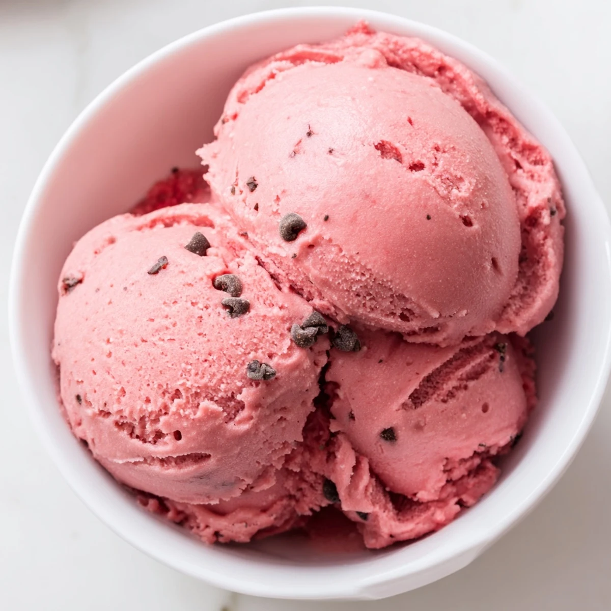 Creamy watermelon ice cream scooped into bowls topped with fresh mint sprigs