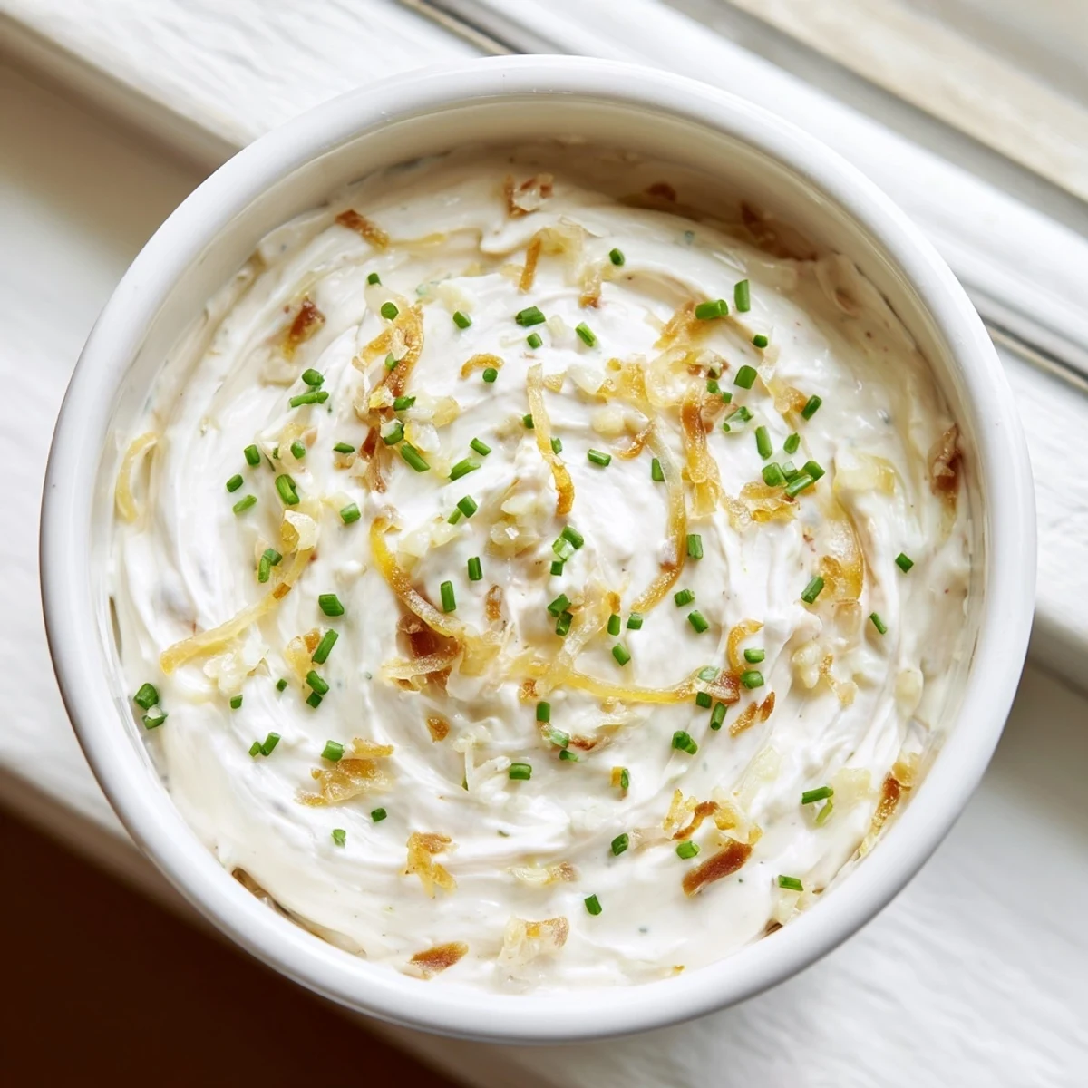 Creamy French onion dip topped with caramelized onions and fresh chives beside potato chips