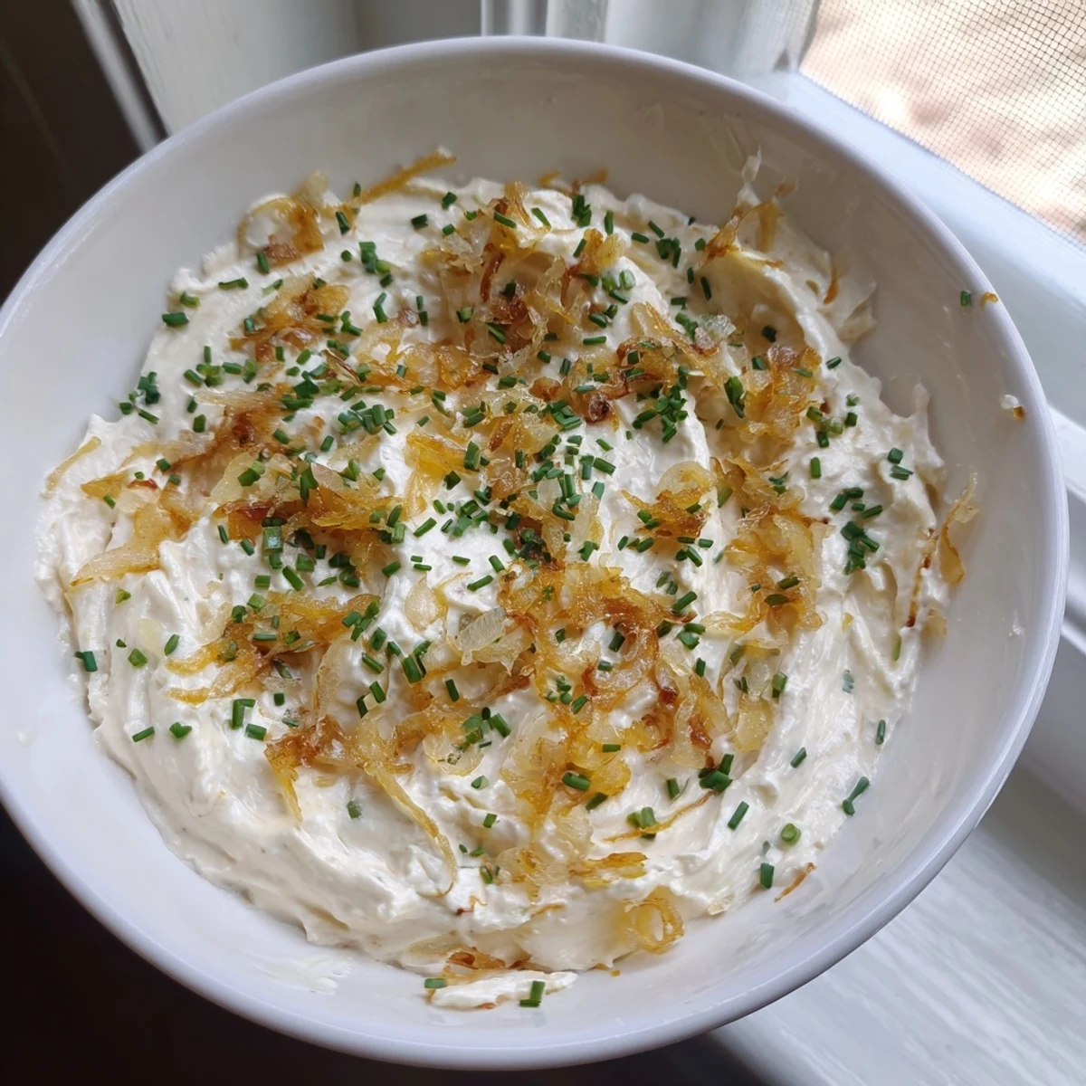 Homemade French onion dip featuring rich caramelized onions garnished with green onions and chips