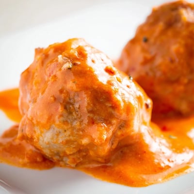 Tender turkey meatballs simmer in a vibrant roasted red pepper sauce inside a skillet, steam rising from the surface.